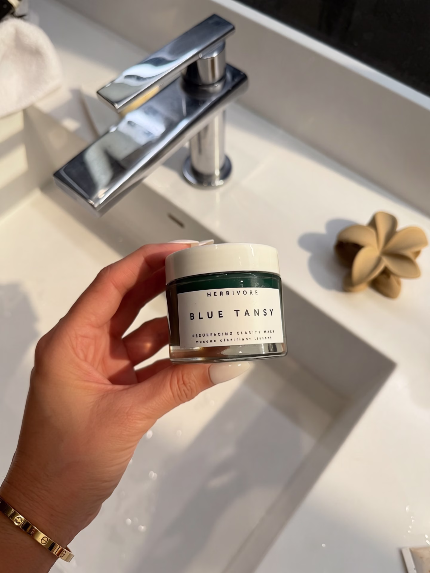 The image features a close-up of a clear glass skincare jar containing a turquoise gel product, likely a blue tansy resurfacing clarity mask, topped with a white lid. This gel mask is designed to gently exfoliate and promote glowing skin, making it suitable for sensitive skin types.