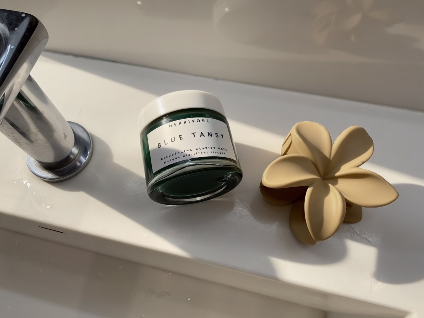 The image features a close-up of a clear glass skincare jar containing a turquoise gel product, likely a blue tansy resurfacing clarity mask, topped with a white lid. This gel mask is designed to gently exfoliate and promote glowing skin, making it suitable for sensitive skin types.