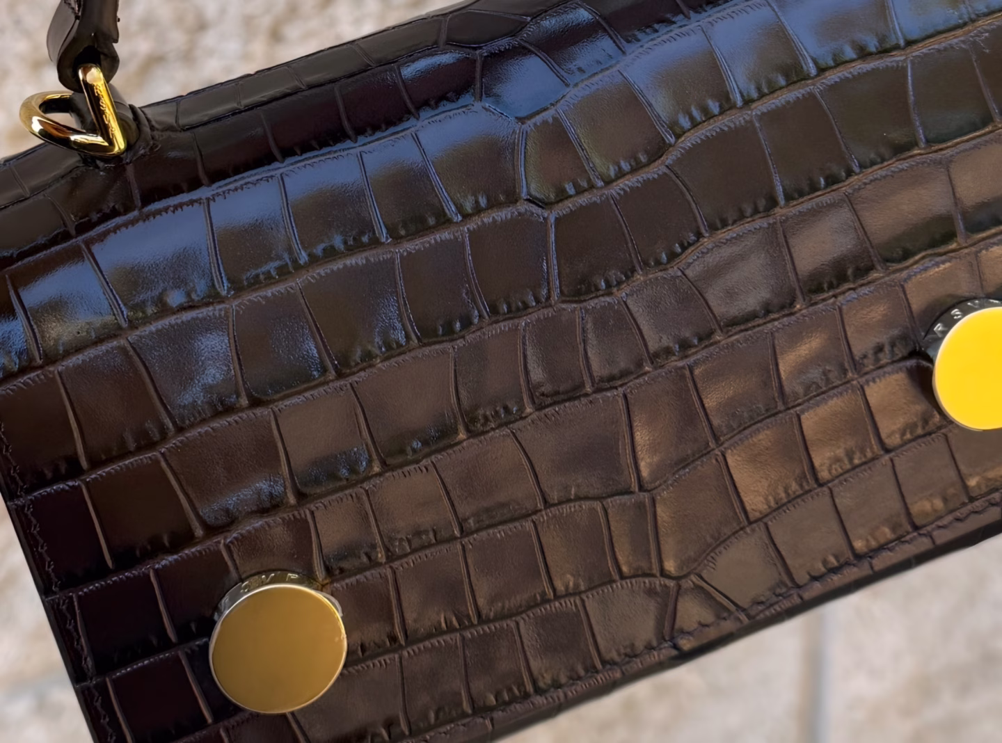 This close-up image showcases the rich texture of a chocolate brown crocodile embossed leather handbag, highlighting its subtle sheen and quality craftsmanship. The luxurious design reflects the elegance associated with RSVP Paris bags, emphasizing both style and functionality.